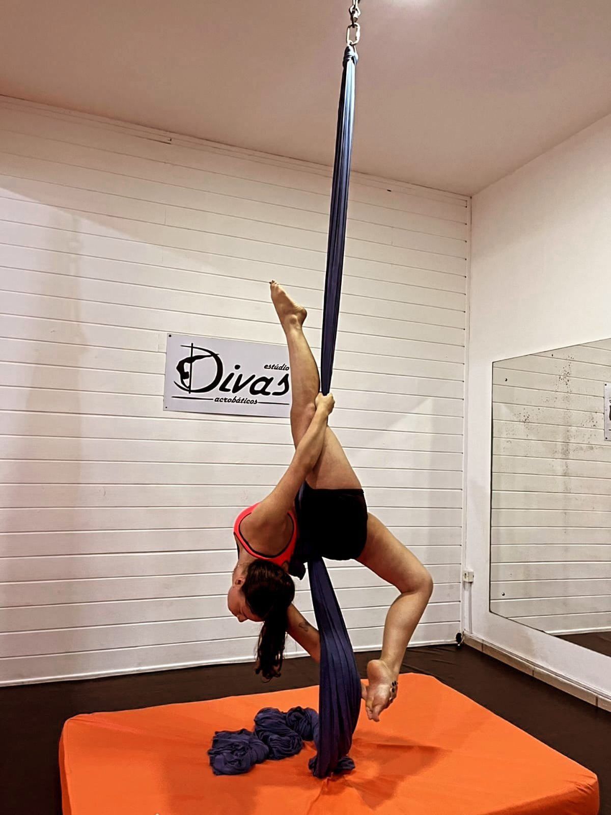 Aluna suspensa em tecido acrobático, pose de escorpião, no Estúdio Divas